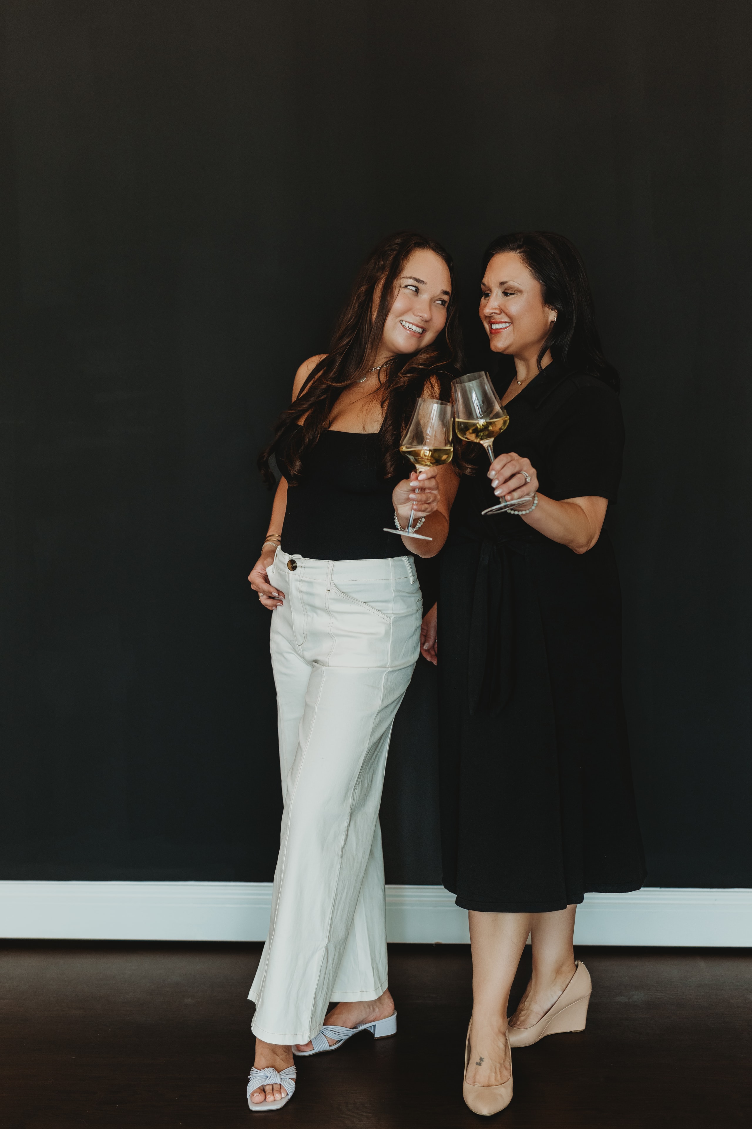 Lauren and Riley with wine glasses against dark background